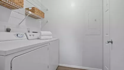 A dedicated laundry space with a white washer and dryer, wire shelving, and neatly folded towels in a bright, minimalist setting.