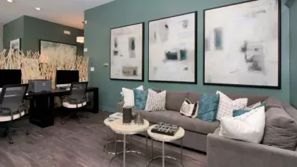A cozy business center with workstations, abstract artwork, and a comfortable gray sectional adorned with decorative pillows.
