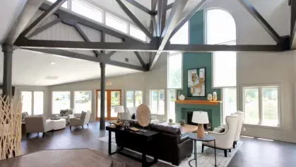 A spacious clubhouse with soaring ceilings, large windows, and a central seating area featuring a fireplace and contemporary furnishings.