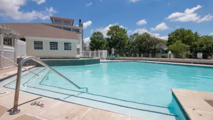 A sparkling swimming pool with built-in steps, a surrounding sundeck, and a modern clubhouse in the background.