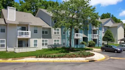A charming apartment complex with well-maintained landscaping, blue and beige exteriors, and private balconies.