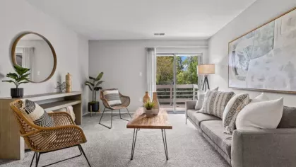 A bright and airy living room with a neutral color palette, textured pillows, and a wooden console table with a round mirror above it.