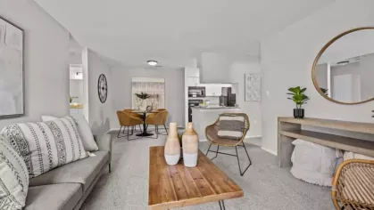 A stylish living space with a gray sofa, a wooden coffee table, a dining area in the background, and rattan accent chairs for a cozy atmosphere.