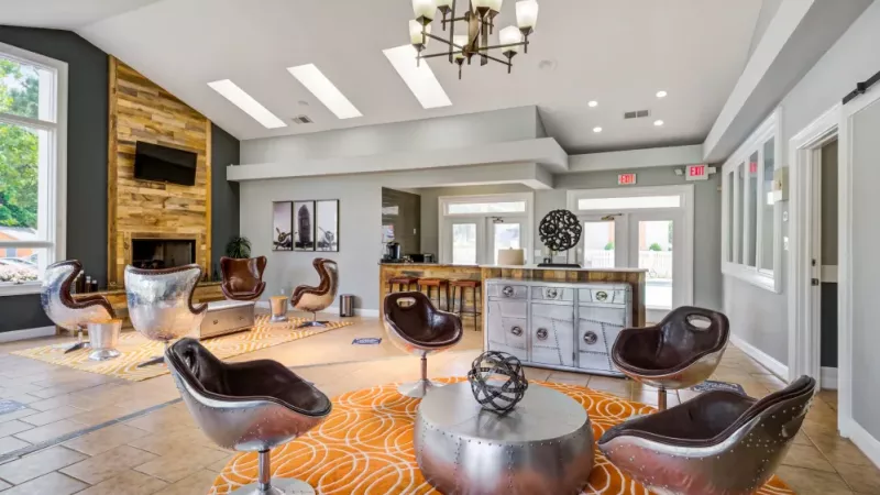 Modern clubhouse lounge with unique metallic chairs and vibrant orange accents.