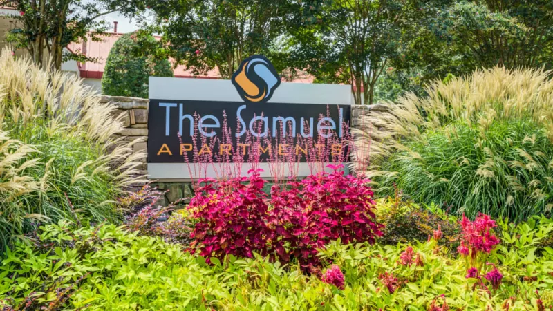 "The Samuel Apartments" sign surrounded by lush landscaping and colorful flowers.
