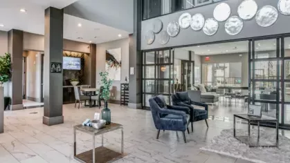 A spacious two-story lobby featuring sleek furnishings, a decorative silver plate installation, and floor-to-ceiling glass doors leading to the lounge.