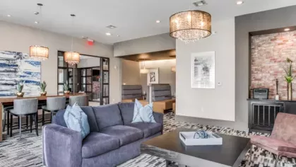 A contemporary social lounge with plush seating, crystal chandeliers, and a mix of workstations and private booths for residents.