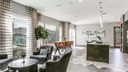 A chic leasing office with modern decor, accent chairs, and a communal table positioned near large windows overlooking the property.