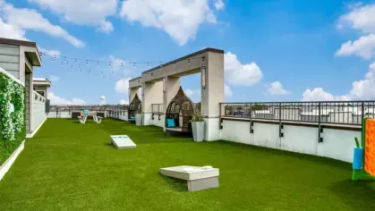 A rooftop lounge with artificial turf, string lights, and shaded seating areas offering a vibrant space for relaxation.