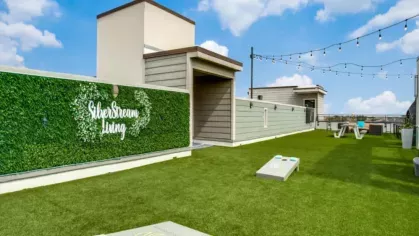 A rooftop recreation area with cornhole boards, picnic tables, and a green wall featuring "SilverStream Living" signage.