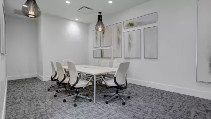 Professional meeting room with a large conference table, white chairs, and modern pendant lighting.