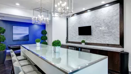 Elegant community kitchen featuring a large glass-top island, modern lighting fixtures, and a sleek design with marble accents.