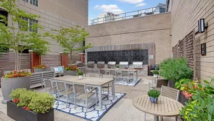 An outdoor grilling and dining space with stainless steel grills, tables, and vibrant greenery for social gatherings.