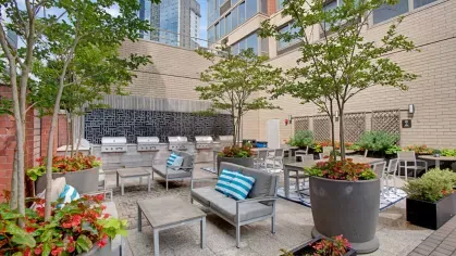 An outdoor grilling and dining space with stainless steel grills, tables, and vibrant greenery for social gatherings.