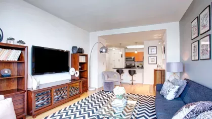 A modern living room with large windows offering city views, stylish furniture, and a bold zigzag patterned rug, creating a vibrant and cozy ambiance.