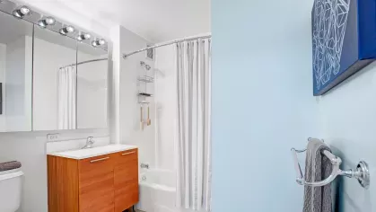 A pristine bathroom with a modern vanity, full-size mirror, and a tiled shower with a curtain, blending functionality with contemporary design.