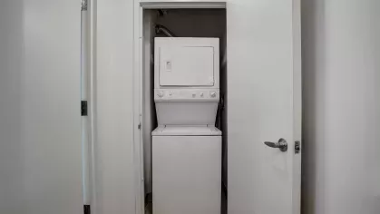 A compact laundry area featuring a stacked washer and dryer unit tucked behind white closet doors, offering convenient in-home laundry access at Skyline New Rochelle Luxury Apartments.