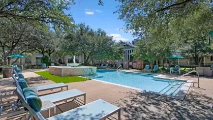 Resort-style pool with comfortable lounge chairs and a central stone water feature.Sparkling pool with a stone water fountain, surrounded by mature trees and sun loungers.