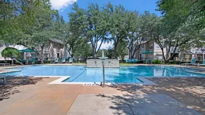 Sparkling pool with a stone water fountain, surrounded by mature trees and sun loungers.