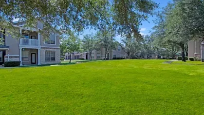 Wide-open green lawn with mature trees and well-maintained apartment buildings in the background.