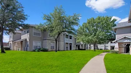 Well-manicured community grounds with a winding sidewalk and mature shade trees.