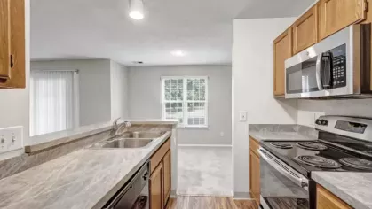 Modern kitchen with stainless steel appliances, wooden cabinetry, and a view of the bright dining area.