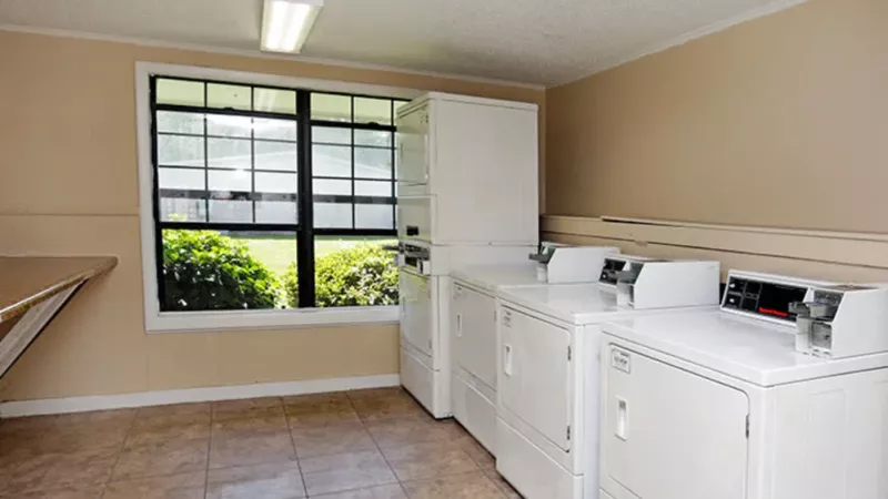 Laundry room with white washing machines and dryers, a large window, and tiled flooring.