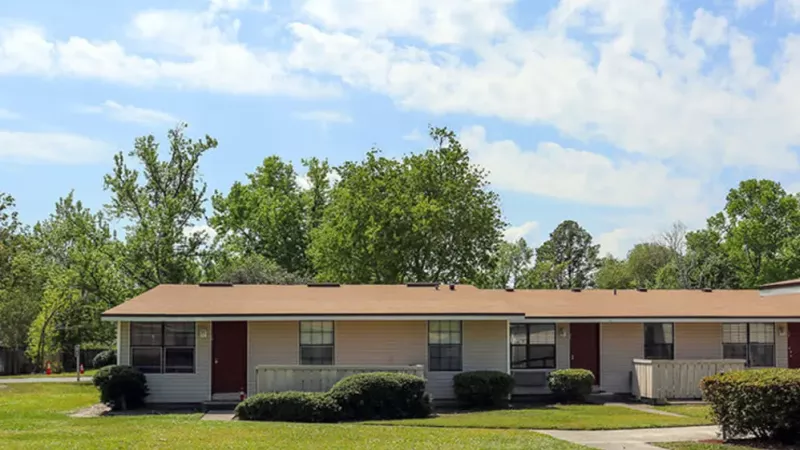 Single-story beige homes with red doors, green lawns, and a clear blue sky.