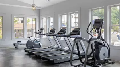 A well-lit gym at Vista At Town Green, featuring state-of-the-art treadmills and ellipticals lined up against large windows with scenic outdoor views.