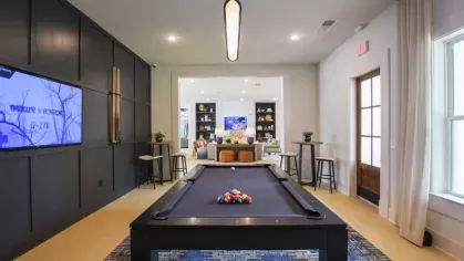 A luxurious entertainment lounge at Vista At Town Green, with a pool table, a large wall-mounted TV, stylish bar stools, and an open concept layout connecting to a cozy seating area.