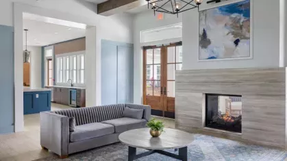A contemporary clubhouse lounge at Vista At Town Green with a sleek grey sofa, a statement fireplace, and modern décor, creating a warm and inviting atmosphere.