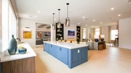 A spacious kitchen area in the clubhouse with a large blue island, modern pendant lighting, and stylish open shelving, perfect for resident events and gatherings.