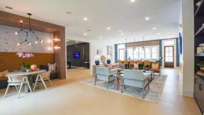 A spacious and elegantly designed resident lounge at Vista At Town Green, featuring stylish seating, a modern kitchen area, and a cozy dining nook with a tufted bench.
