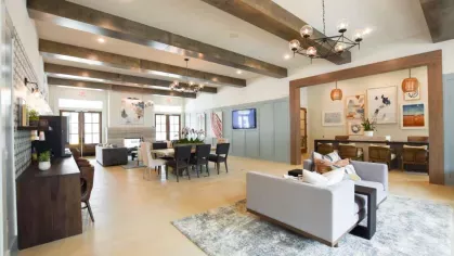 A sophisticated clubhouse featuring high ceilings, stylish furniture, a large communal table, and a fireplace, offering a warm and welcoming ambiance.
