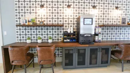 A stylish coffee bar area in the clubhouse with a patterned tile wall, modern lighting, and comfortable leather chairs, perfect for a morning coffee or casual work session.