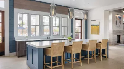 A sophisticated community kitchen with a navy and wood-accented design, high-top seating, and modern light fixtures, offering a luxurious shared space for residents.
