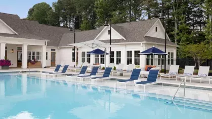 A resort-style swimming pool with luxurious lounge chairs, blue umbrellas, and a modern clubhouse, creating a perfect spot for relaxation at Vista At Town Green.