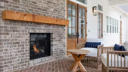 A cozy covered patio with a brick fireplace, comfortable wicker seating, and wooden accents, offering a warm and inviting outdoor retreat.