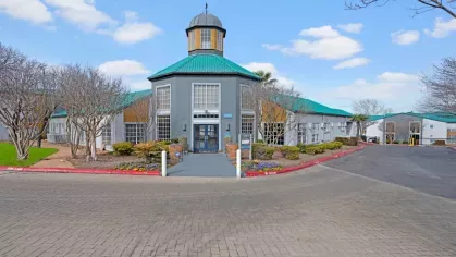 The Clara Apartments clubhouse with a distinctive teal roof and landscaped entrance.