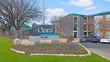 The Clara Apartments sign surrounded by colorful flowers and well-maintained greenery.