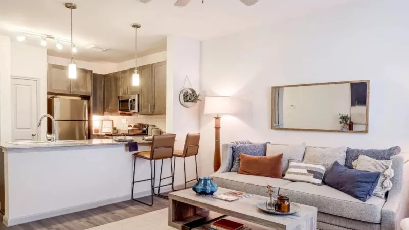 Open-concept living area with a cozy seating arrangement and a view of the contemporary kitchen at The Emerson at Forney.