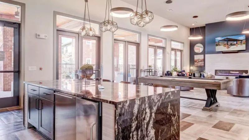 Elegant clubhouse kitchen with a luxurious marble island, modern lighting, and access to the community lounge at The Emerson at Forney Luxury Apartments.