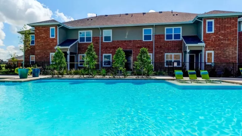 Resort-style swimming pool surrounded by red-brick apartment buildings and lush greenery at The Emerson at Forney Luxury Apartments.