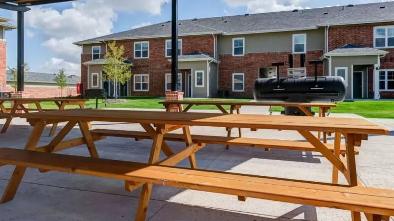 Covered outdoor dining area with picnic tables and a large grill at The Emerson at Forney Luxury Apartments.