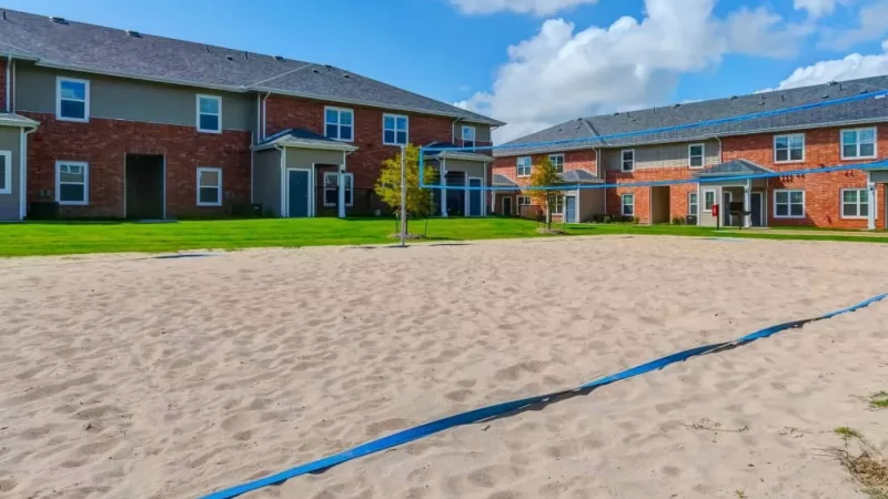 Sandy volleyball court surrounded by green lawns and charming red-brick townhomes at The Emerson at Forney Luxury Apartments.