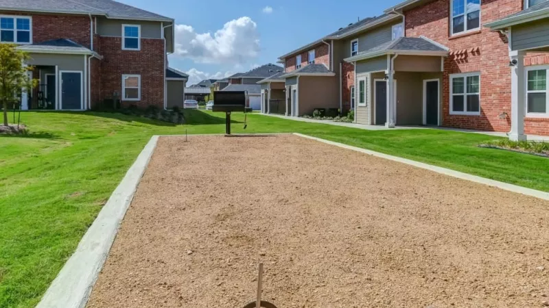 Outdoor horseshoe pit with well-kept landscaping and red-brick apartment exteriors at The Emerson at Forney Luxury Apartments.
