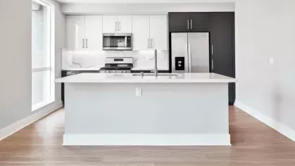 Modern kitchen at The Linden Luxury Apartments featuring white and black cabinetry, stainless steel appliances, and a spacious island with quartz countertops.