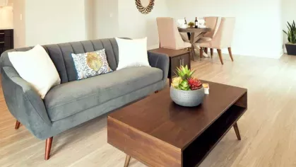 Living area at The Linden Luxury Apartments with a modern grey couch, wood coffee table, and elegant dining space with light beige chairs.