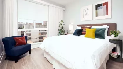 Bright bedroom at The Linden Luxury Apartments featuring a cozy bed with colorful pillows, modern artwork, and natural light from a large window.