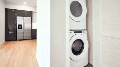 In-unit laundry at The Linden Luxury Apartments with a stacked washer and dryer set, conveniently located near the kitchen area.